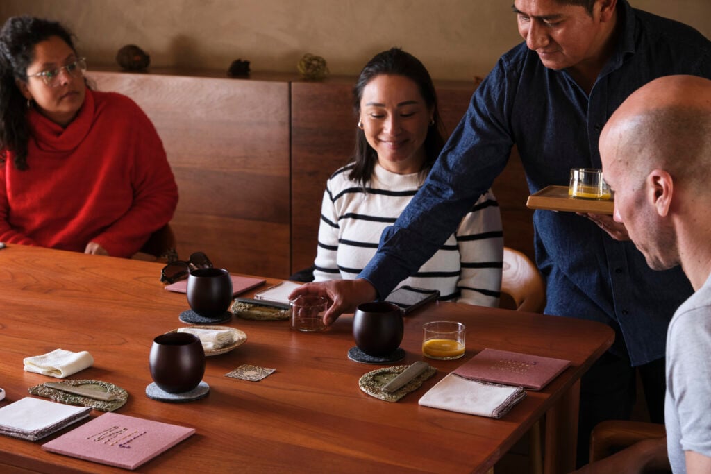 A smiling woman seated around a wooden table in a fine dining restaurant receives a beverage.