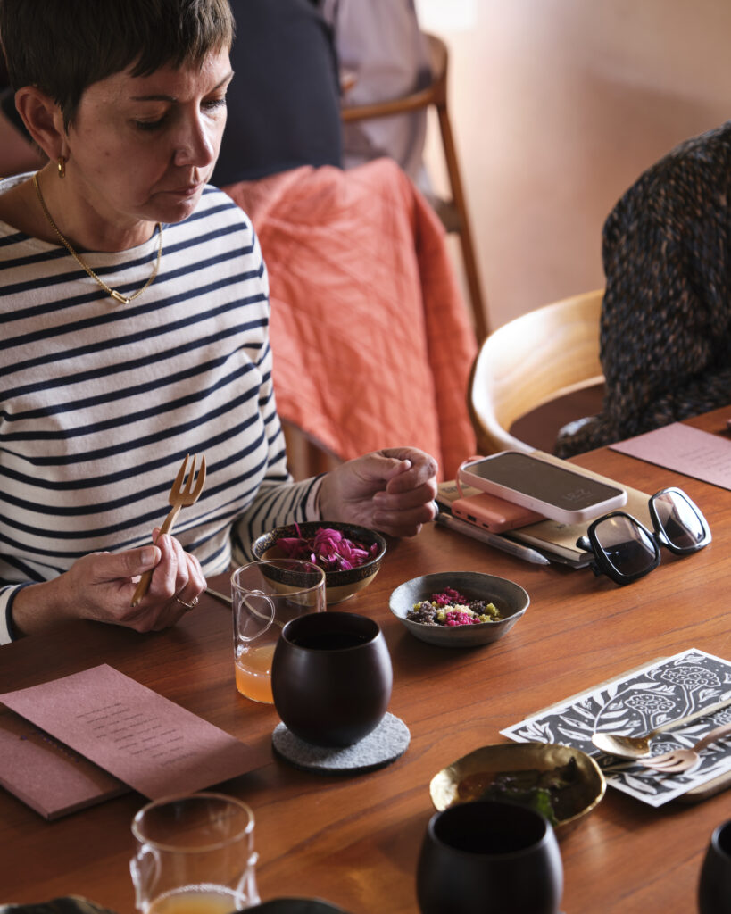 A woman in a white and blue striped shirt is sitting at a wooden table, eating a restaurant meal from several ceramic bowls