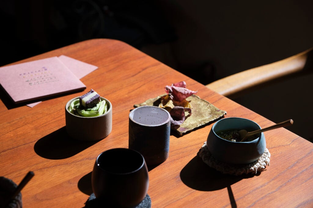 ceramic cups and small plates sit atop a wooden table, each filled with a different morsel of food