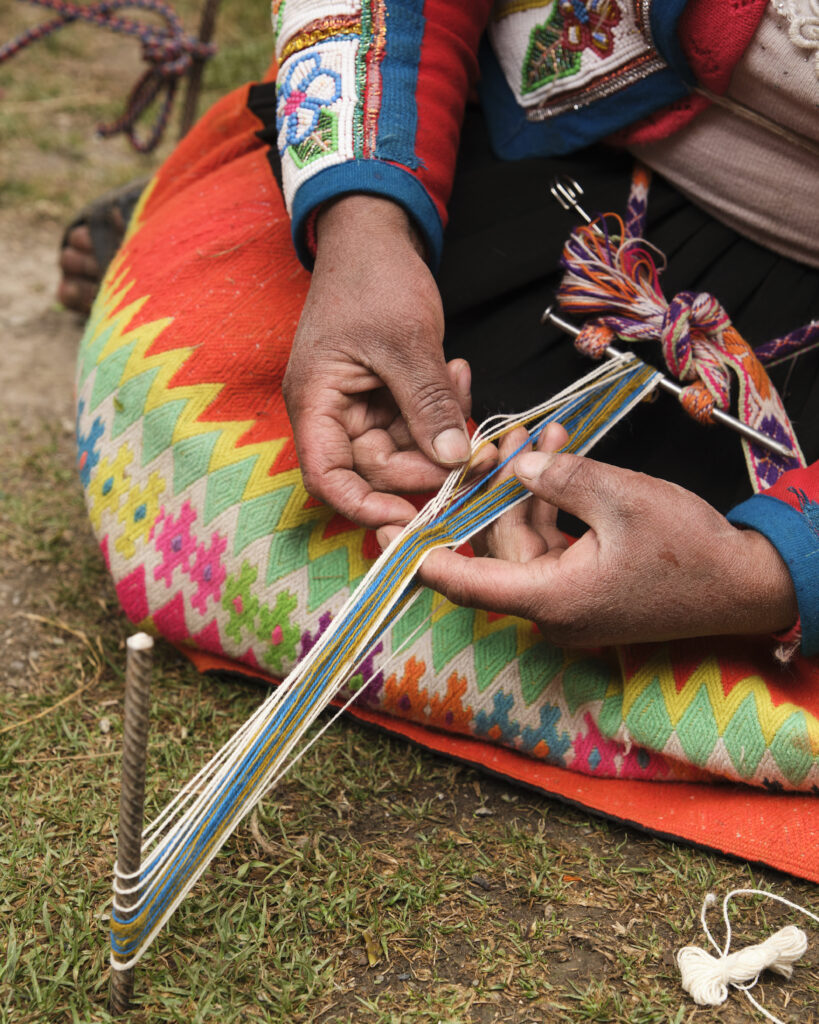 A pair of hands holding a weaving tool, creating multi-colored fiber art.